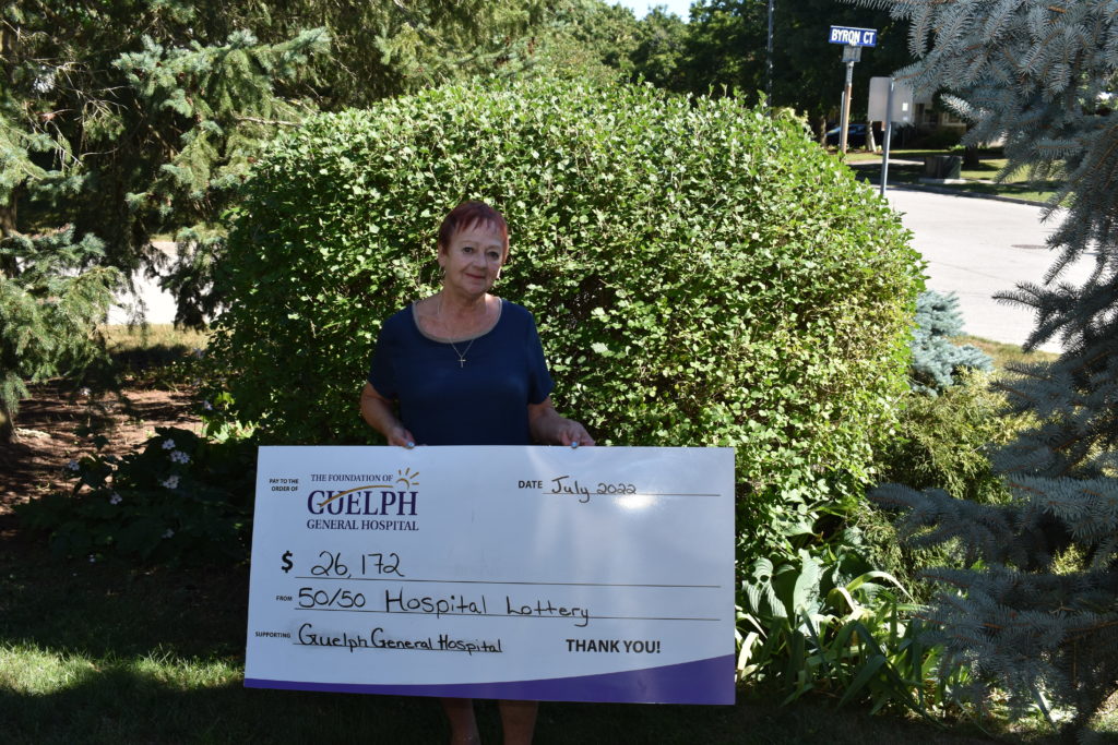 Winner, Helen holding up a big cheque of $26,172 in her garden.